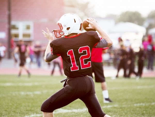 Rear View Of Quarterback Throwing Football On Playing Field